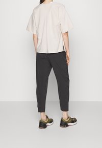 Beige kortärmad topp med en avslappnad passform, kombinerad med mörka cargobyxor. Skorna har en grön och svart design med vadderade sålar.