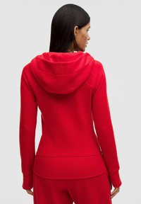 Červená mikina s kapucí z měkkého materiálu, s kapucí na stažení a jemným logem. Přiléhavý střih s žebrovanými detaily na lemu a manžetách.