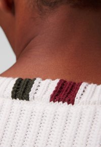 Maglione all'uncinetto con un corpo bianco e un motivo testurizzato. Accentuato all'collo con righe verdi, borgogna e bianche.