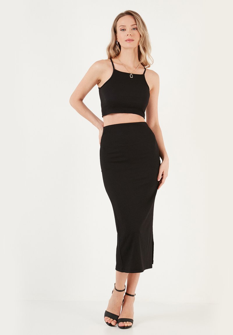 Crop top noir à fines bretelles associé à une jupe midi ajustée. Texture lisse avec un léger détail en côtes. Des sandales à talons hauts noires complètent l'ensemble.