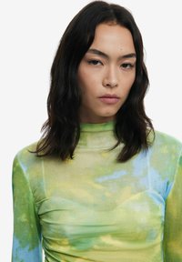 Top a maniche lunghe e collo alto realizzato in tessuto testurizzato con un motivo tie-dye verde, giallo e blu. Presenta dettagli arricciati sui lati.