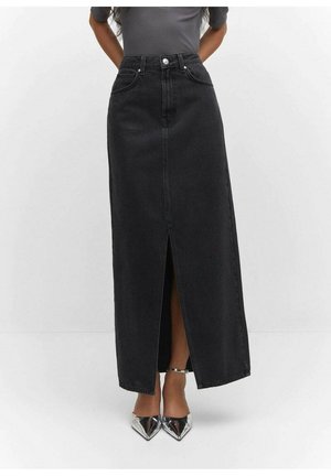 Frau trägt einen schwarzen Denim-Maxirock mit hoher Taille und Frontschlitz, kombiniert mit silbernen spitzen High Heels und einem grauen, gerippten Oberteil.