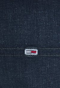 Mörk denimtyg med en subtil textur. Inkluderar en liten, broderad logotyp med färgerna röd, vit och blå på en söm.