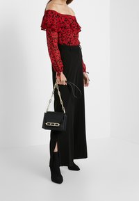 Blouse rouge à fleurs, décolletée à volants, associée à un pantalon noir à jambes larges. Accessoires comprenant un petit sac noir avec une chaîne dorée.