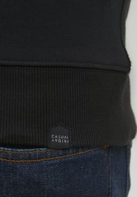 Fekete pamut pulóver bordázott textúrával és szegéllyel, 'CASUAL FRIDAY' felirattal fehér színben, sötét háttéren.