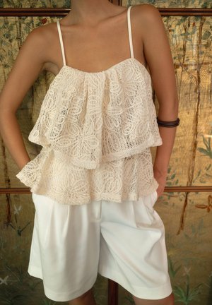 Lace camisole in cream with layered frill design, featuring thin straps and intricate floral patterns, paired with loose white shorts.