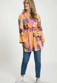 Kleurrijke gestreepte kimono met klokmouwen, een getailleerde taille en zakken. Draagt over een paarse top en gecombineerd met gescheurde jeans en witte sneakers.