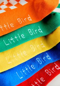 Barvne nogavice v oranžni, zeleni, rumeni, modri in rdeči barvi z belim napisom "Little Bird". Pleteno blago z rebrasto teksturo.