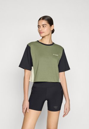 Cropped T-shirt featuring green, black, and beige color blocks, short sleeves, and a logo on the chest. Paired with black shorts.