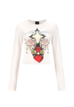 Camisa corta de manga larga blanca con un gran cruz, un corazón rojo, flores amarillas y un diseño de mariposa en el frente, además de texto en cursiva arriba.