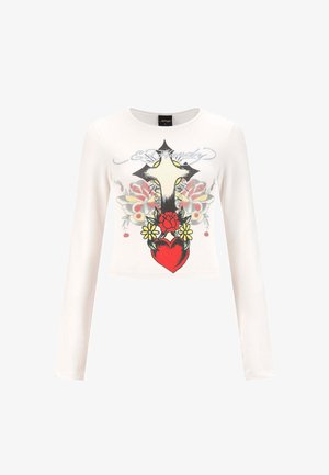 Camisa corta de manga larga blanca con un gran cruz, un corazón rojo, flores amarillas y un diseño de mariposa en el frente, además de texto en cursiva arriba.