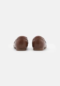 Mocassins en cuir marron avec un bout arrondi et un talon bas. Texture lisse avec des détails de couture minimes et une finition légèrement brillante.
