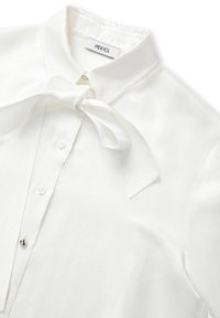 Biała bluzka o fakturowanym wykończeniu, z kołnierzykiem w szpic, wiązaną kokardą na szyi i zapięciem na guziki. Marka: IPEKYOL.