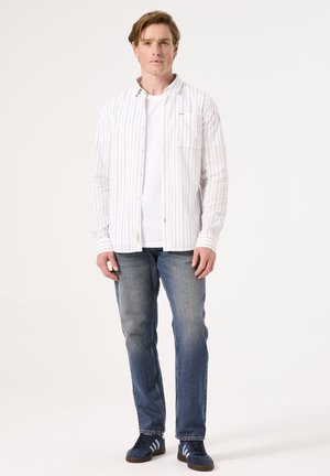 Wit gestreepte overhemd over een wit T-shirt, gecombineerd met blauwe jeans en marineblauwe schoenen met lichtblauwe strepen. Eenvoudig, casual ontwerp.