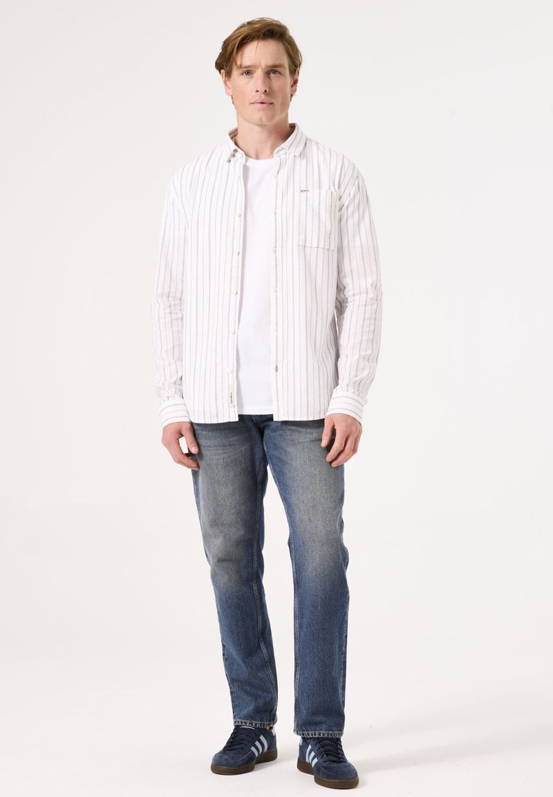 Camisa de botones blanca a rayas sobre una camiseta blanca, combinada con vaqueros azules y zapatos navy con rayas azul claro. Diseño simple y casual.
