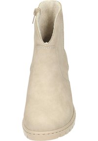 Bottine beige avec une tige en simili cuir lisse, bout rond, accents cousus et une fermeture éclair sur le côté pour un enfilage facile. Semelle plate et texturée.