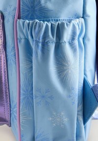 Sac à dos bleu clair avec un motif de flocons de neige, présentant une poche latérale froncée et des accents violets. Fabriqué en matériau synthétique texturé.