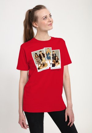 Ung kvinde med hestehale iført en rød T-shirt med fotos af seks stilfuldt klædte personer og teksten "Skandaløse Liv blandt Manhattans Elite."