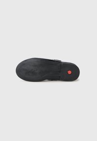 Schwarze Schuhsohle mit eingeprägtem "Pom d’api", rotes Granatapfel-Logo nah an der Ferse, vor einem schlichten weißen Hintergrund präsentiert.