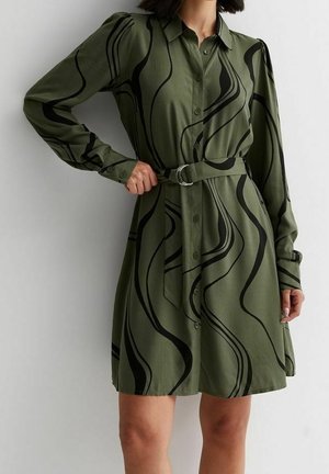Robe chemise vert olive à manches longues avec motifs abstraits noirs en forme de tourbillon, boutonnage à l’avant, col et ceinture en tissu avec boucle métallique.