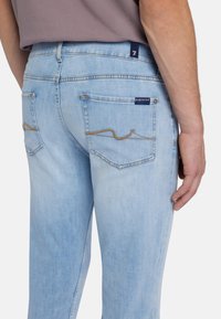 Jeans in denim azzurro chiaro con una finitura sbiadita, dotati di due tasche posteriori e cuciture arancioni in un motivo ondulato.