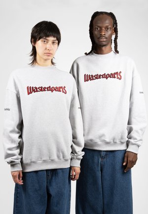 Sudaderas grises con el logo de "Wastedparts" en rojo, que presentan puños y dobladillos acanalados. Combinadas con pantalones de mezclilla de corte holgado. Diseño sencillo y casual.