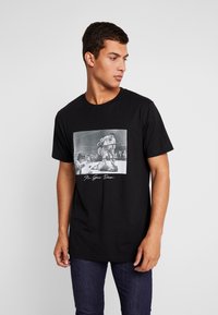 T-shirt en coton noir arborant un imprimé graphique de sport vintage sur le devant, avec un texte blanc en dessous. Manches courtes et col rond.