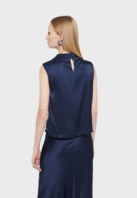 Námornícky modrý saténový top bez rukávov s detailom v tvare kľúčovej dierky na zadnej strane a rovnými okrajmi. Má hladkú textúru a mierny lesk.