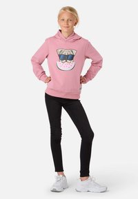Rosa hoodie med en hundillustration med solglasögon, tillsammans med svarta leggings och vita sneakers. Enkelt mönster, mjukt tyg.