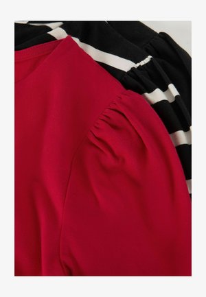 Piros és fekete laza felsők, amelyek puha pamut anyagból készültek, puffos ujjakkal, a fekete változaton csíkos mintázattal.