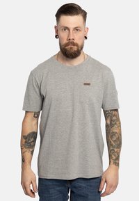 T-shirt in cotone grigio con maniche corte, colletto rotondo e tasca sul lato sinistro del petto. Dettaglio distintivo con etichetta marrone sulla tasca. Vestibilità casual.