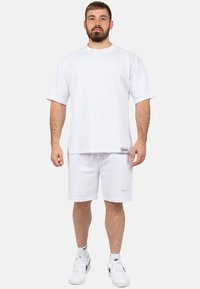 Witte katoenen T-shirt met korte mouwen en een ronde halslijn, gecombineerd met witte shorts. Inclusief logo-accenten op het shirt en de shorts.