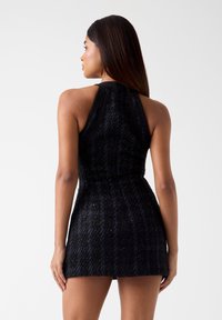 Schwarzes Neckholder-Kleid aus strukturiertem, schimmerndem Stoff. Es verfügt über eine taillierte Passform und einen ausgestellten Rock, der eine elegante Silhouette betont.