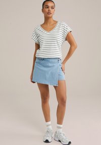 Randig vit och svart t-shirt med kort ärm, parat med en ljusblå denim omlottskjol som har en sidoknäppning och fickor.