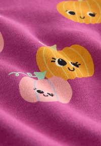 Lila Stoff mit verspielten Illustrationen von orangefarbenen und rosa Kürbissen mit lächelnden Gesichtern, verziert mit grünen Ranken und Akzenten.