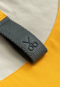Katoenen tas met een gele paneel en een grijze geweven handgreep met een zwart schaarembleem. Soepele textuur, gestructureerde vorm en contrasterende kleuren.