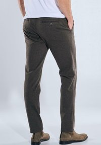 Dark brown tailored trousers with a smooth texture, featuring rear pockets and minimal detailing, paired with light brown ankle boots.