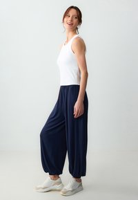 Canotta bianca a righe abbinata a pantaloni harem larghi di colore blu navy. La modella indossa sneakers bianche con dettagli beige, che mettono in risalto un look rilassato.
