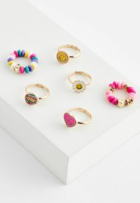 Fünf Ringe auf einer weißen Oberfläche präsentiert: Ein Perlenring mit bunten Scheiben, dazu vier Metallringe mit Smiley-Gesichtern und floralen Designs.