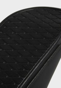 Černá podešev obuvi s texturovaným povrchem a diamantovým vzorem, vyrobená z gumy. Okraj je hladký s mírným leskem.