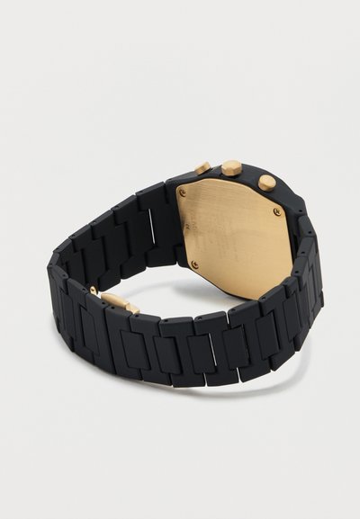 Μαύρο μεταλλικό ρολόι χειρός με συνδεδεμένους κρίκους, χρυσή πίσω θήκη και τρία χρυσά κουμπιά στο πλάι, τοποθετημένο σε λευκή επιφάνεια.