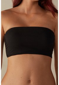 Musta bandeau-toppi, joka on tehty sileästä kankaasta. Yksinkertainen muotoilu ilman olkaimia, suora pääntie ja saumoista vapaat reunat.