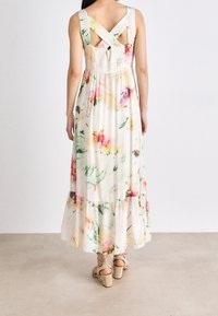 Robe maxi florale en tissu léger, avec un ourlet en couches, des bretelles croisées dans le dos et un motif aquarelle multicolore avec des accents de verdure.