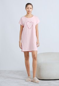 Ροζ βαμβακερό νυχτικό με κοντά μανίκια, διακοσμημένο με σχέδιο καρδιάς από επαναλαμβανόμενο κείμενο. Μαλακό ύφασμα και άνετη εφαρμογή.