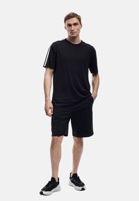 Schwarzes Sport-T-Shirt mit kurzen Ärmeln und weißen Seitenstreifen, kombiniert mit schwarzen Shorts. Leichtes Material, klassischer Rundhalsausschnitt und figurbetonter Schnitt.