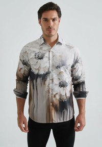 Chemise à manches longues à boutons en tissu léger, arborant un motif floral en blanc et noir avec des accents abstraits marron.