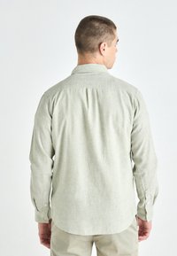 Light green long-sleeve shirt made of textured fabric, featuring a collar, button cuffs, and a curved hem with a yoke detail.