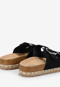 Sandales en suède noir avec une semelle en liège, dotées d'une semelle en jute, de deux sangles latérales et de boucles en métal pour un ajustement réglable.