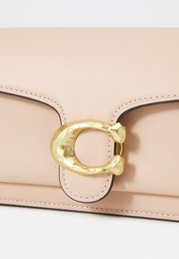 Clutch din piele roz, cu închidere din metal aurit, având un accent distinctiv în formă de C și detalii de cusătură subtile.
