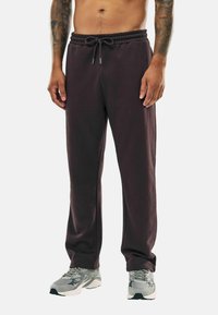 Braune Jogginghose mit elastischem Bund, Kordelzug, seitlichen Taschen und gerippten Säumen, kombiniert mit grauen Sportschuhen.